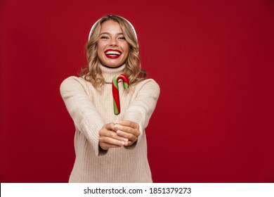 Lovely happy young woman wearing santa hat posing with candy cane isolated over red background