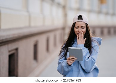 Lovely Hispanic Brunette Casual Dressed Walking In The City, Makes Video Call,woman Holding A Tablet, Watching Videos, Series. Touches The Face In Surprise. Talking With Friend.  Conversation Concept