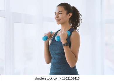 Lovely Hispanic woman doing exercises with dumbbells indoors, empty space