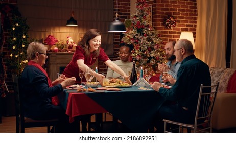 Lovely housewife bringing main course to Christmas dinner table. Impatient and happy festive family members gathered at home to celebrate winter holiday with traditional home cooked food. - Powered by Shutterstock