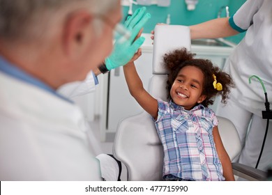 Lovely kid in dental chair with dentist satisfied after repairing teeth