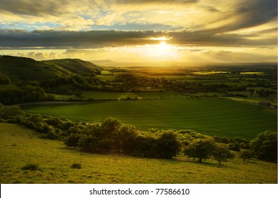 Lovely landscape of countryside hills and valleys with setting sun lighting up side of hills whit sun beams through dramatic clouds - Powered by Shutterstock