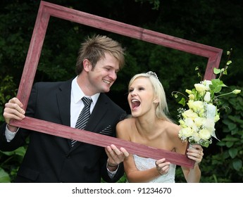 Lovely Laughing Wedding Couple Looking Through A Wooden Picture Frame
