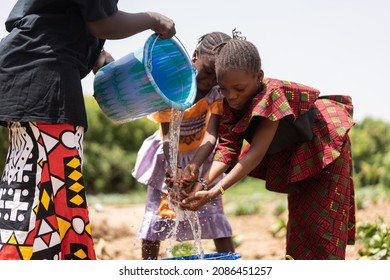 Lovely little black African girls washing their hands with clear fresh well water water flowing from a bucket