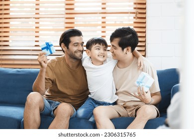 Lovely little boy gives fathers a present in the father's day festival, happy Asian and Caucasian gay couple with foster son. A diversity in gender - LGBTQ and ethnicity concept.