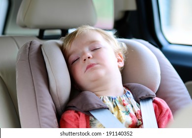 Lovely Little Child, Cute Blonde Curly Toddler Girl Peacefully Sleeping In The Car Sitting In A Baby Seat With Belt Enjoying A Family Vacation Trip In A Modern Safe Vehicle