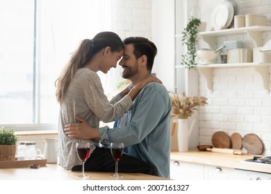 Lovely married couple in love touch foreheads while spend time together at modern home enjoy romantic dating in kitchen with red wine. Romance, anniversary celebration, life event, relations concept