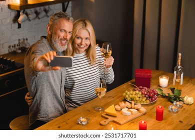 Lovely mature couple taking selfie having romantic date in the kitchen. Vlogging blogging on St Valentine`s Day, anniversary celebration. Online social media posting, videocall - Powered by Shutterstock