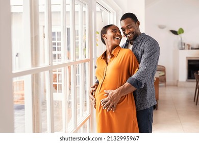 Lovely mid black man hugging his pregnant wife from behind standing near window at home. Happy middle aged black husband embracing pregnant woman while waiting for baby. African american mature couple - Powered by Shutterstock