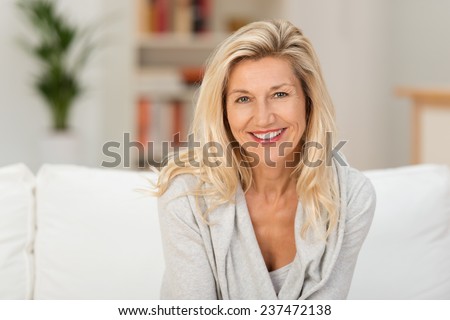 Lovely middle-aged blond woman with a beaming smile sitting on a sofa at home looking at the camera