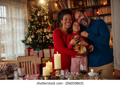 Lovely mixed race parents and little girl standing in the living room near dining table. It is Christmas time and they are celebrating together - Powered by Shutterstock