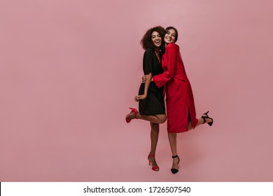 Lovely modern woman in bright red midi dress and dark heels hugging her smiling friend with curly hair and black clothes. - Powered by Shutterstock