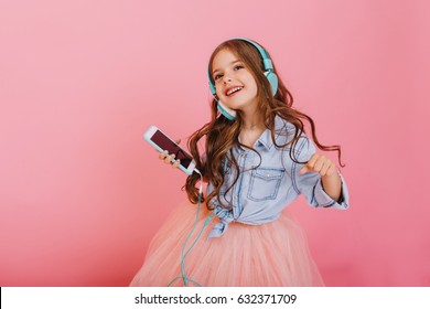 Lovely Moments Of Little Child Enjoying Music Through Headphones, Dancing With Phone Isolated On Pink Background. Expressing True Positive Emotions Of Fashionable Happy Child At Entertainment