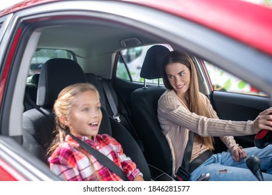 Lovely Motherhood. Smiling Mom Driving With Her Lovely Girl Sitting On Passenger Seat