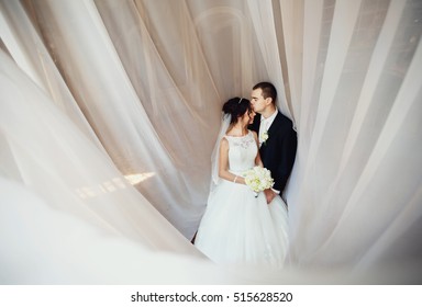 Lovely newlyweds under the white curtains