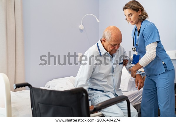Lovely nurse\
assisting senior man to get up from bed at hospital. Caring nurse\
supporting elderly patient while getting up from bed and move\
towards wheelchair at nursing home.\
