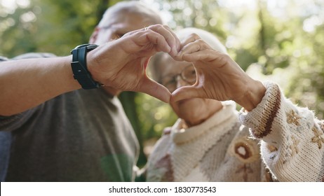 Lovely Older Retired Couple Making Heart With Their Hands And Looking At Each Other. Selective Focus.  