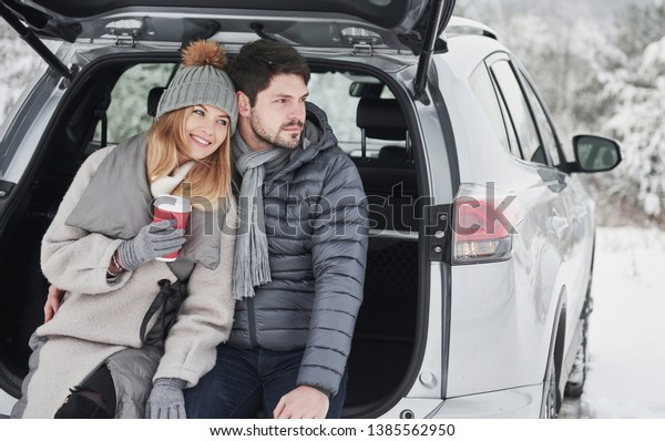 Lovely people.\
Nice couple have weekend at countryside at winter time. Sitting on\
the rear part of modern\
car.