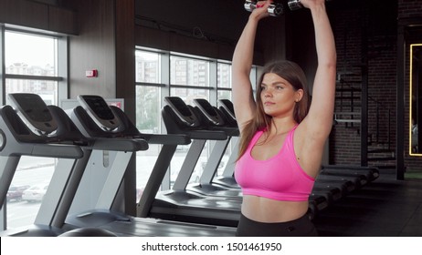 Lovely Plus Size Sportswoman Smiling To The Camera After Lifting Weights At The Gym. Charming Curvy Woman Enjoying Exercising At The Gym, Lifting Dumbbells. Workout, Body Positive Concept