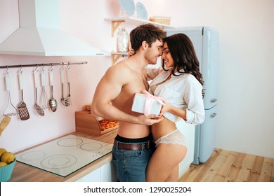 Lovely romantic couple stand in kitchen close to each other. They smile and look at each other. People have box with present.