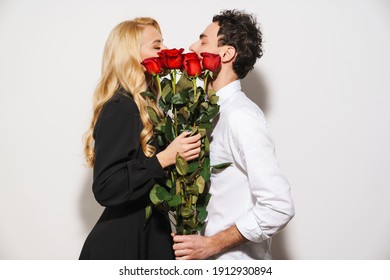 Lovely romantic young happy couple celebrating an event together, woman holding bouquet of red roses isolated over white background, kissing - Powered by Shutterstock