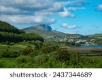 Lovely seaside town of Portree with majestic Old Man Of Storr in the background. Iconic natural attraction towering above charming village. Dramatic landscape on magnificent Scottish Isle of Skye.