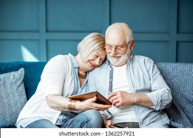 Lovely senior couple dressed casually using digital tablet while sitting together on the comfortable couch at home - Powered by Shutterstock