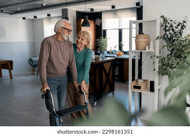 Lovely senior couple in retirement at home. Supportive wife taking care of husband with physical disability, helping him to walk around with mobility walker. Happy elderly couple in love. - Powered by Shutterstock