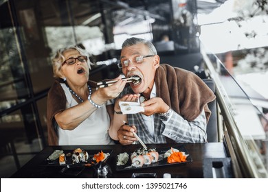 Lovely Seniors Couple Eating Sushi With Red Fish And Sitting At Summer Terrace