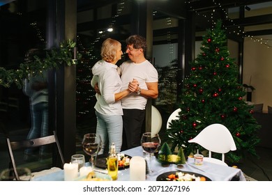 Lovely Sixty Year Old Couple Dancing Next To A Dining Table And A Christmas Tree. Having Together Time After A Celebration.