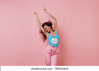 Lovely slim girl posing with sincere smile. Pretty long-haired female model dancing with hands up on pink background.