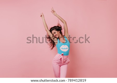 Lovely slim girl posing with sincere smile. Pretty long-haired female model dancing with hands up on pink background.