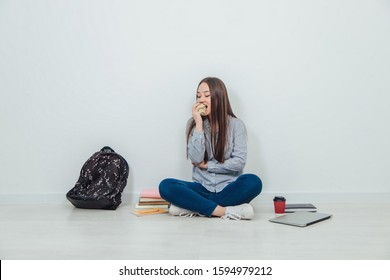 Lovely Smiling Asian Student Girl Sitting On The Floor In Lotos Position, Eating An Apple. A Lot Of School Supplies Around Her.