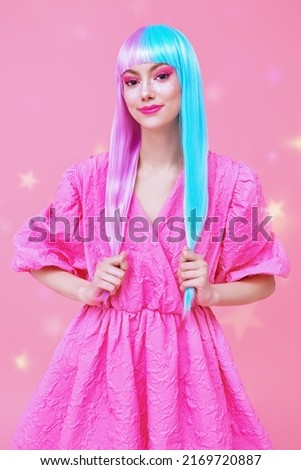 A lovely, smiling girl with colored purple-blue hair and pink dress poses on a pink background with magic stars. Hairstyle, hair coloring. Make-up and cosmetics. 