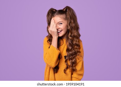 Lovely Smiling Shy Teen Girl In Yellow Knitted Sweater Hiding Half Of Face With Hand And Looking At Camera Against Violet Background