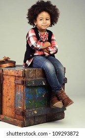 Lovely stylish little girl sitting on an old wooden box
