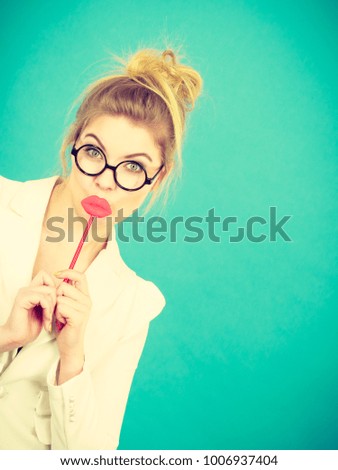 Lovely sweet business woman elegant clothing nerdy glasses holding red fake lips on stick having fun, on blue green. Photo take and carnival funny accessories concept.