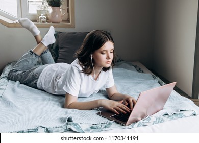 Lovely teenage girl 12-16 years old, at home sitting \ lying on the bed, communicating with friends on the laptop. Teen girl doing homework on laptop.