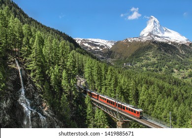 Lovely view of the Matterhorn. A train crossing an old bridge and a waterfall in front of the mountain. Zermatt, Switzerland. Summer in the alps.