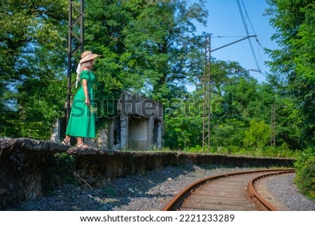 a lovely woman in a green dress is walking by the railway