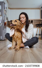 Lovely Woman Playing With Her Dog And Taking Care Covering It In A Blanket And Hugging The Pet At Home