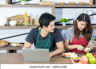 Lovely Young Asian Couple In Kitchen, Business Owner Man Looks At Wife While She Is Slicing Fresh Fruit For Husband, Preparing Healthy Food For Good Health And Diet. Medical Healthcare Concept.