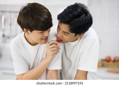 Lovely Young Asian Gay Man Feeding Apple To His Partner At Kitchen During Cooking Salad. LGBT Men Together. Healthy Eating Lifestyle For Same Sex Family In Valentine's Day.