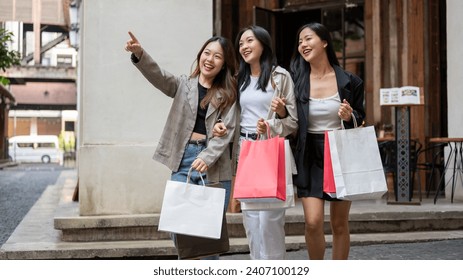 Lovely young Asian girl friends are walking with their shopping bags, enjoying shopping day in the city together. Travel abroad, tourist, consumerism, fashion and lifestyle - Powered by Shutterstock