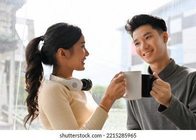 Lovely young Asian office-couple standing by the window, having afternoon coffee break together. - Powered by Shutterstock