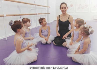Lovely young ballerina enjoying teaching ballet class to her little students. Group of adorable little girls listening to their ballet teacher. Education, childhood concept