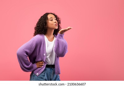 Lovely young black woman blowing air kiss at camera over pink studio background, copy space. Portrait of pretty African American lady being flirty, sending her love. Valentine's Day concept