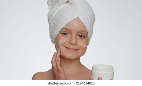 Lovely Young Child Girl With Towel On Head Applying Cleansing Moisturizing Cream From Creme Jar. Teenager Kid Face Skincare Healthy Treatment, Natural Cosmetics. Female Portrait. Perfect Fresh Clean