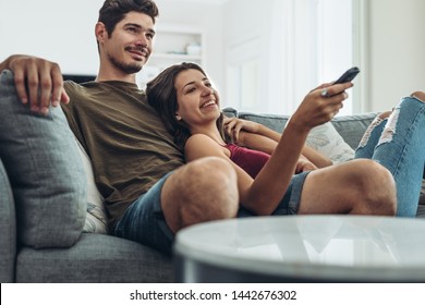 Lovely young couple relaxing at home enjoying a television program. Man and woman relaxing on sofa watching television together at home.