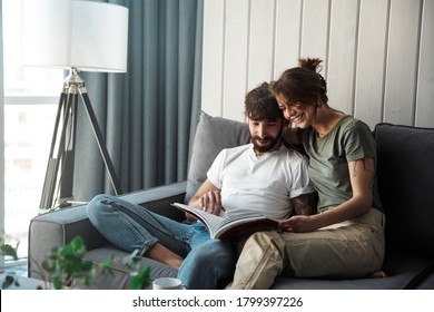 Lovely Young Couple Relaxing On A Couch At Home, Reading Magazine